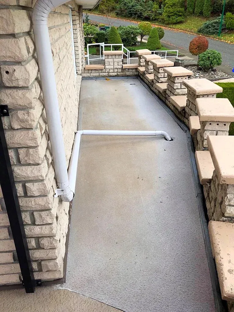 White drain piping running from a downspout across a balcony floor