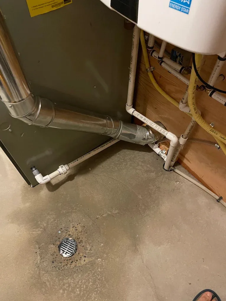 White PVC condensate piping running to a basement floor drain beside a furnace