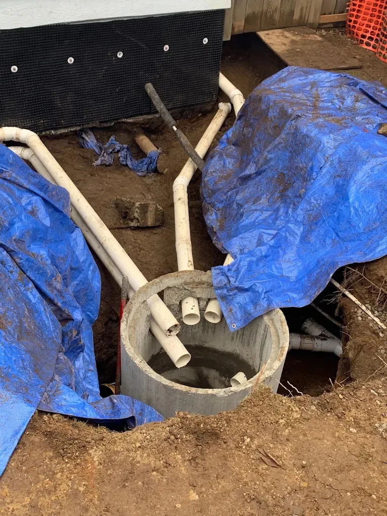 Concrete drainage pit with several PVC pipes connected beside a foundation wall