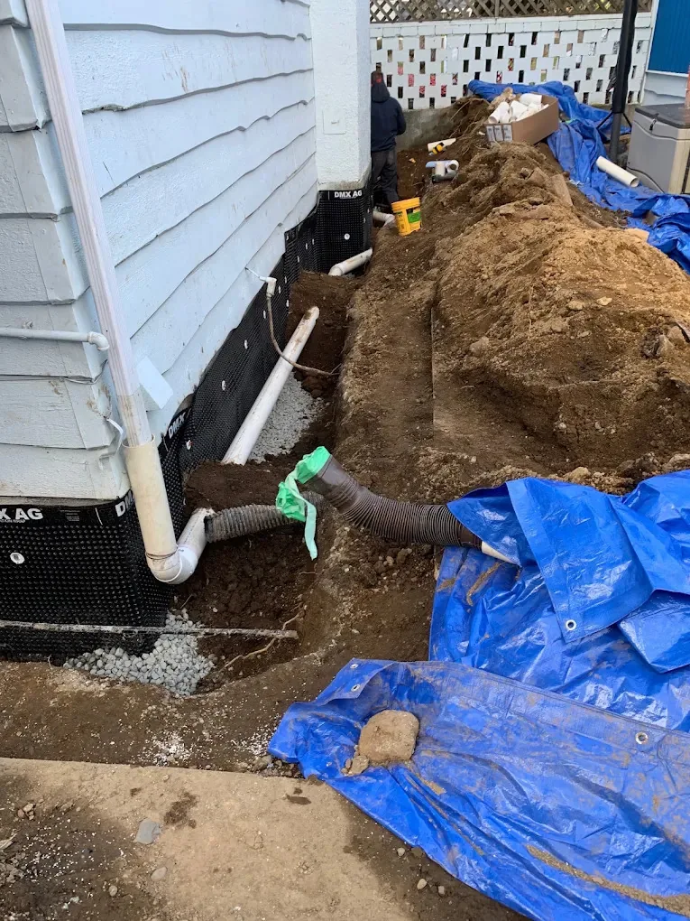 Foundation drainage pipe and gravel beside a house wall covered with dimpled membrane