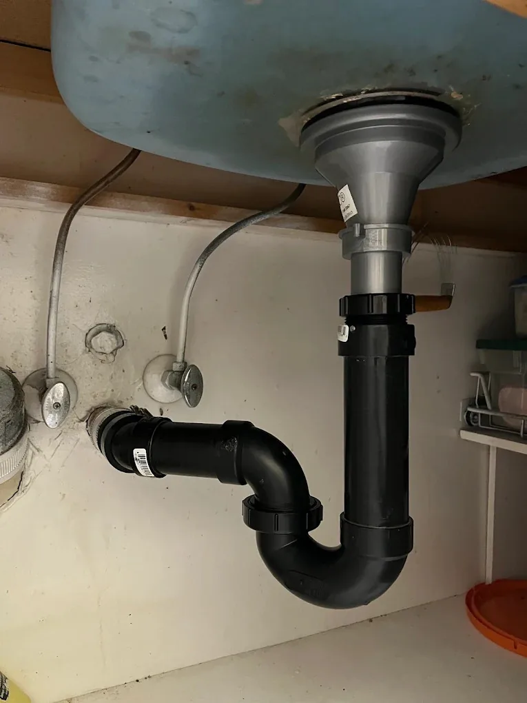 Black drain trap and pipes under a kitchen sink after replacement